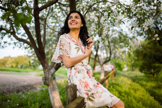 Vertical photo of a happy girl enjoying spring scenery. Woman in a blooming garden park. Rural landscape.