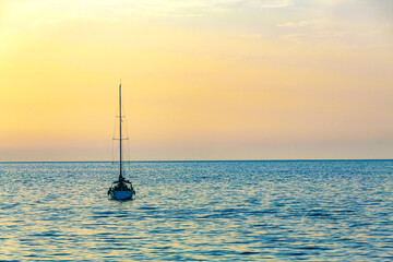 Serene seascape with a sailboat at dusk, basking in the gradient hues of the sunset across the calm sea