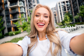Fototapeta premium Selfie photo of charming funky lady in blue shirt shooting herself lick teeth demonstrate residential complex she rent apartment outdoors