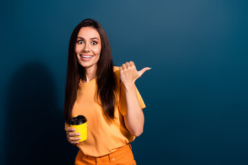 Portrait of excited woman wear orange t shirt direct finger coffee shop holding paper cup espresso isolated on dark blue color background