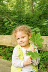 Smiling little girl holding green maple leaves in her hands. Happy childhood. Children's Day. Portrait of a European girl.