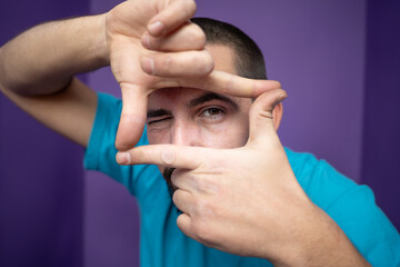 Young handsome man doing frame using hands palms and fingers, over purple background. High quality photo