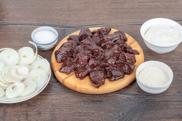 Slices of beef liver, onion rings, salt and sour cream on a wooden table.