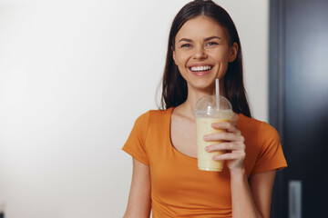 Happy young woman enjoying a refreshing smoothie and smiling at the camera in a health and wellness concept