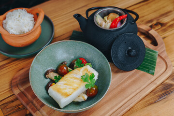 A plate of food with a fish and vegetables sits on a wooden board