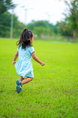 Adorable toddler asian girl enjoying walk and run on green grass in city park sunset light