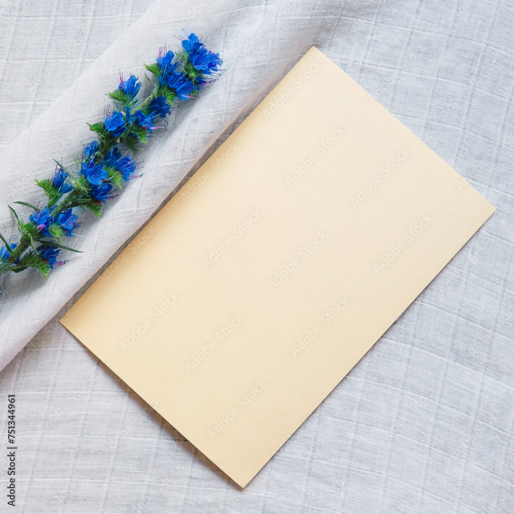 Poster Paper card for text on a linen white tablecloth, decorated with a branch of fresh blue flowers