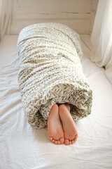 Rolled person. A child wrapped in a blanket with sticking out feet lies on the bed in the bedroom. Sunny morning dream. Psychology comfort. Top view. High quality