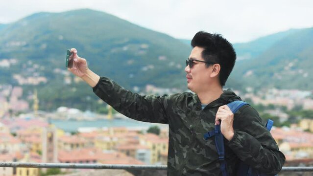 Happy young Asian tourist man selfie by mobile smartphone, Male traveller taking photo, recording vlog on holiday vacation trip at italy.