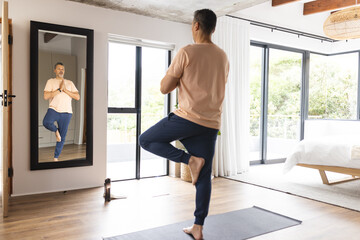 Biracial senior man practices yoga in a bright, modern bedroom