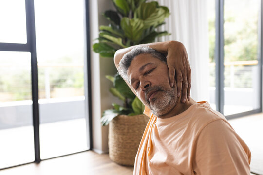 Biracial senior man with grey hair appears to have neck pain, wearing a casual orange shirt