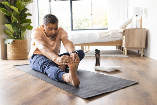 Biracial senior man stretches on a yoga mat at home