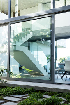 A modern staircase is visible through the large glass window of a contemporary house