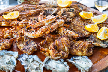 Grilled mix seafood on wooden plate. Charcuterie platter board with shrimp, oysters, fish, squids and octopus in fish restaurant. Healthy diet food