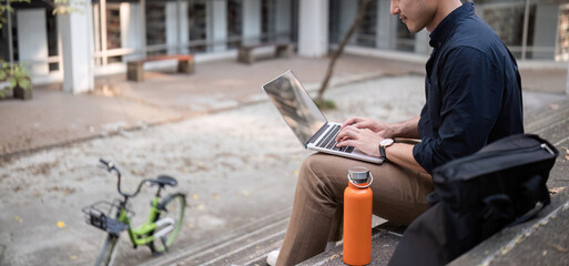 A young Asian businessman rides a bicycle to work. Sitting outside the office working using a...