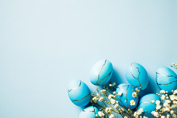 Painted Easter eggs and spring flowers on a blue background. Top view, flat lay.