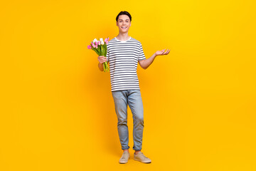 Full size photo of nice student dressed striped t-shirt hold tulips palm presenting promo empty space isolated on yellow color background