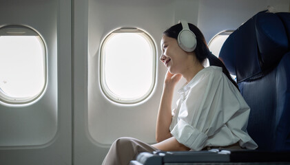 Young woman wearing headphones listening to music during travel, sitting near window in first class...