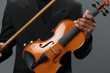 Fototapeta premium Elegant musician in black suit holding violin and bow on gray background in studio setting