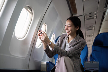 Young female traveler sits near the window in first class on a plane during a flight. Use your cell phone to take photos of the view outside your window, travel, and business ideas.