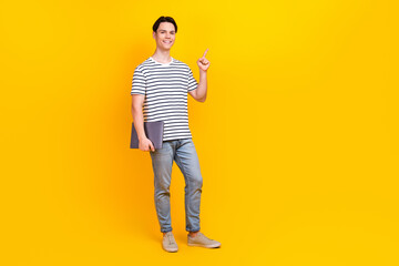 Full size photo of clever student dressed striped t-shirt hold laptop indicating at sale empty space isolated on yellow color background