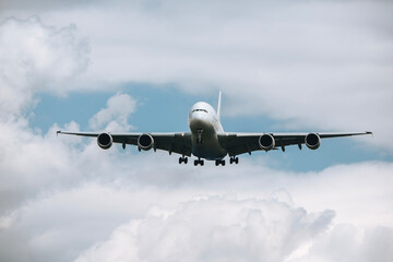 Huge airplane flying through clouds. Plane approaching during landing at airport on sunny day..