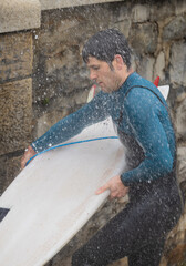 Surfer washing surfboard at outdoor beach shower.