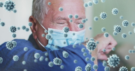 Image of covid 19 cells over man wearing face mask