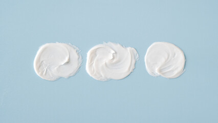 cosmetic smears white cream texture on blue background, top view