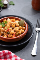 Homemade Ropa vieja, typical Canarian dish of chickpeas stew with chicken and potatoes in a earthenware casserole on marble table. Vertical format.