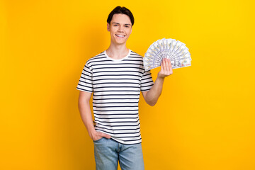 Photo of cheerful guy with brunet hair dressed striped t-shirt holding bunch of dollars arm in...