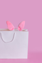 Easter bunny ears in a white paper bag on a pink background, vertical.