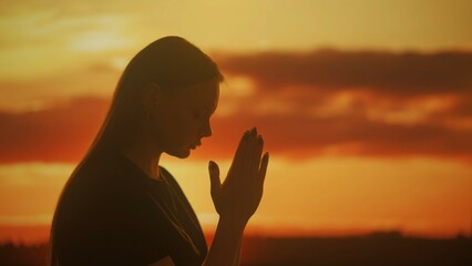 Silhouette of a female praying at sunset