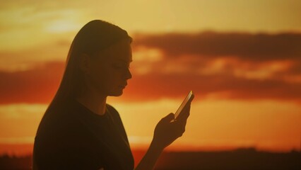Silhouette of a female with a smartphone at sunset