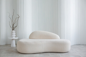 A cute soft white sofa against the backdrop of a foliated wall made of cylinders and a vase with...