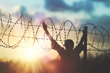 a person raising their arms up behind a barbed wire fence - obrazy, fototapety, plakaty