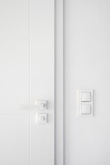 Closed modern room door with white handle and light switch on wall at apartment