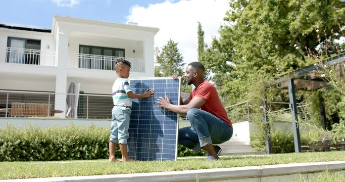 African American father and son examine a solar panel outdoors at home