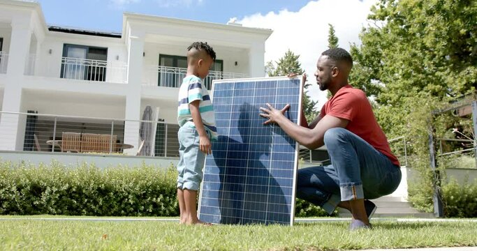 African American father and son examine a solar panel outdoors at home