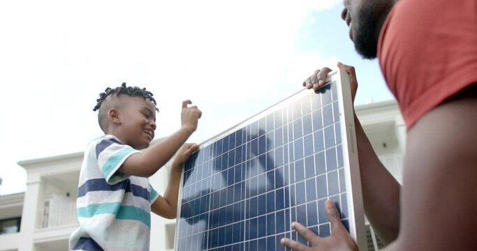 African American father and son handle a solar panel outdoors at home