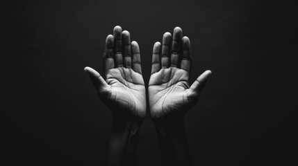 Prayerful hands open towards the sky in black and white image. Black background with open palms...