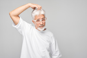 Confident senior man with glasses posing on a gray background.