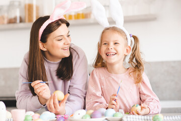 Smiling woman decorating Easter eggs wearing bunny headbands at home close up. Holiday season.