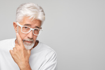 Senior man with white hair and glasses looking thoughtful, isolated on a grey background.