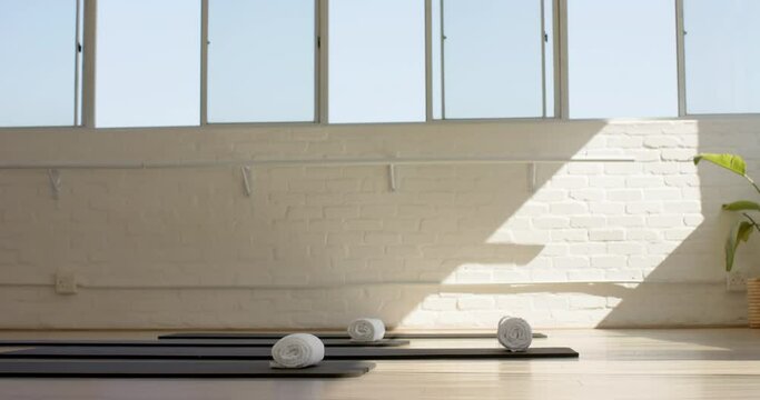 Sunlight filters through large windows onto yoga mats and rolled towels with copy space