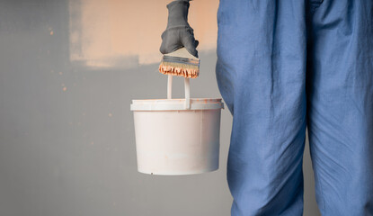 Close-up of a painter with a bucket and brush standing near the wall. Wall painting tool concept. © Andrii Lysenko