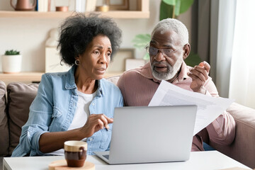 Senior couple checking and calculate financial billing together on sofa. Mature couple discussing their monthly expenses at home. Elderly couple keeping an eye on their finances.  - obrazy, fototapety, plakaty