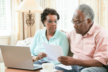 Senior couple checking and calculate financial billing together on sofa. Mature couple discussing their monthly expenses at home. Elderly couple keeping an eye on their finances.  - obrazy, fototapety, plakaty