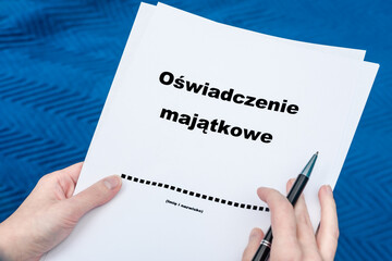 Oświadczenie majątkowe i dlugopis trzymane w dłoniach, napisy w języku polskim