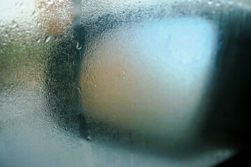 Autospiegel hinter nasser beschlagener Glasscheibe mit Eis- und Wassermuster am Morgen im Winter